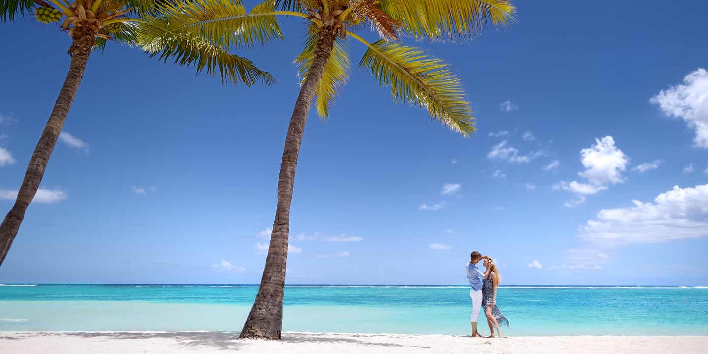 Paar am weißen Sandstrand mit zwei Palmen und hellblauem Wasser