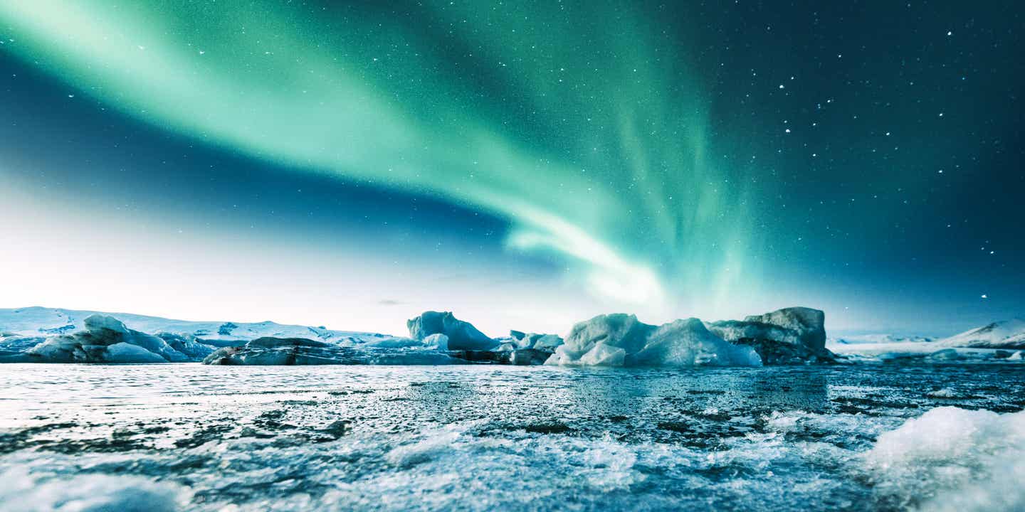Polarlichter über der Gletscherlagune Jökulsárlón in Island mit leuchtenden Eisbergen und nächtlichem Sternenhimmel  