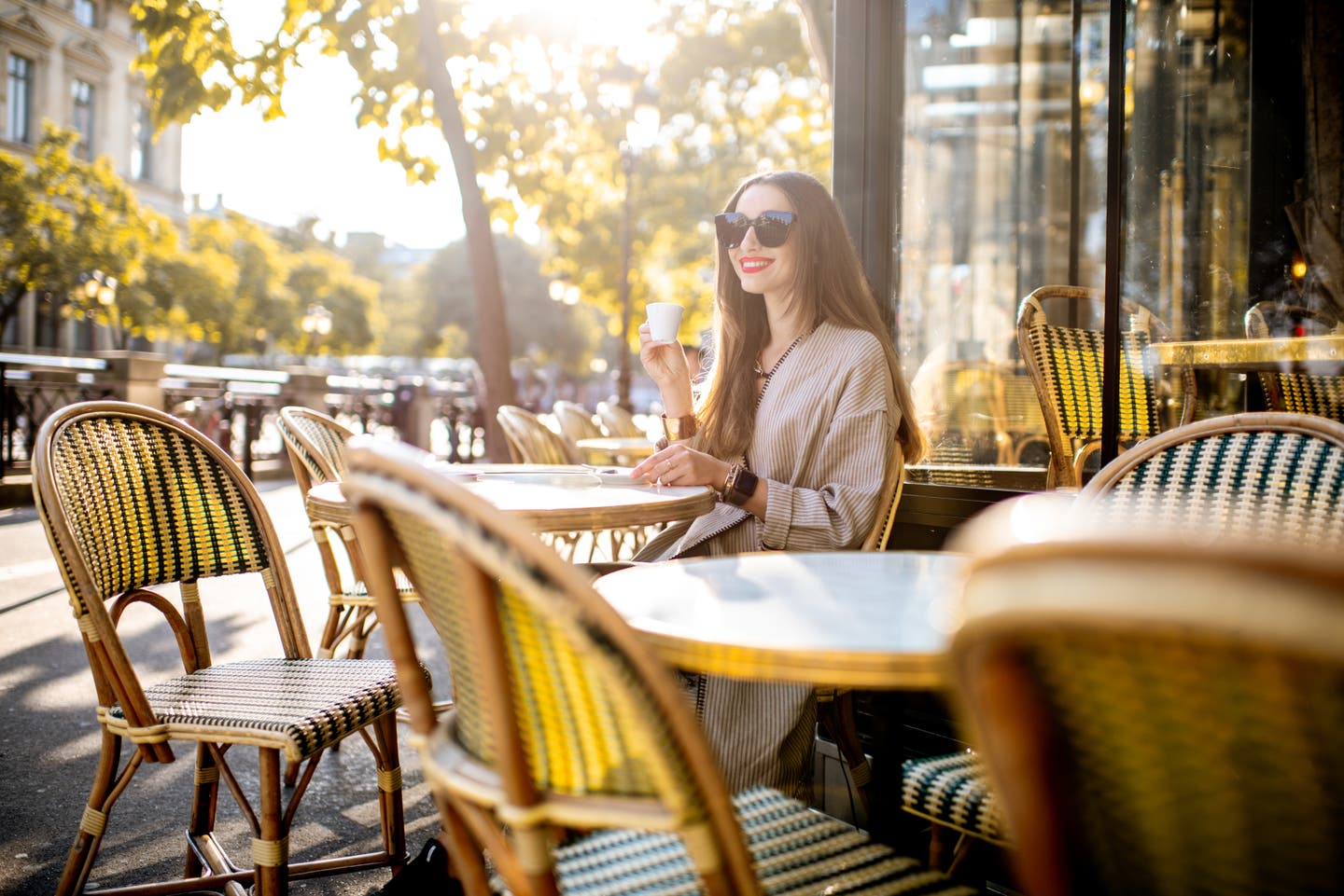Eine strahlende Frau mit Sonnenbrille genießt einen Kaffee in einem Pariser Café