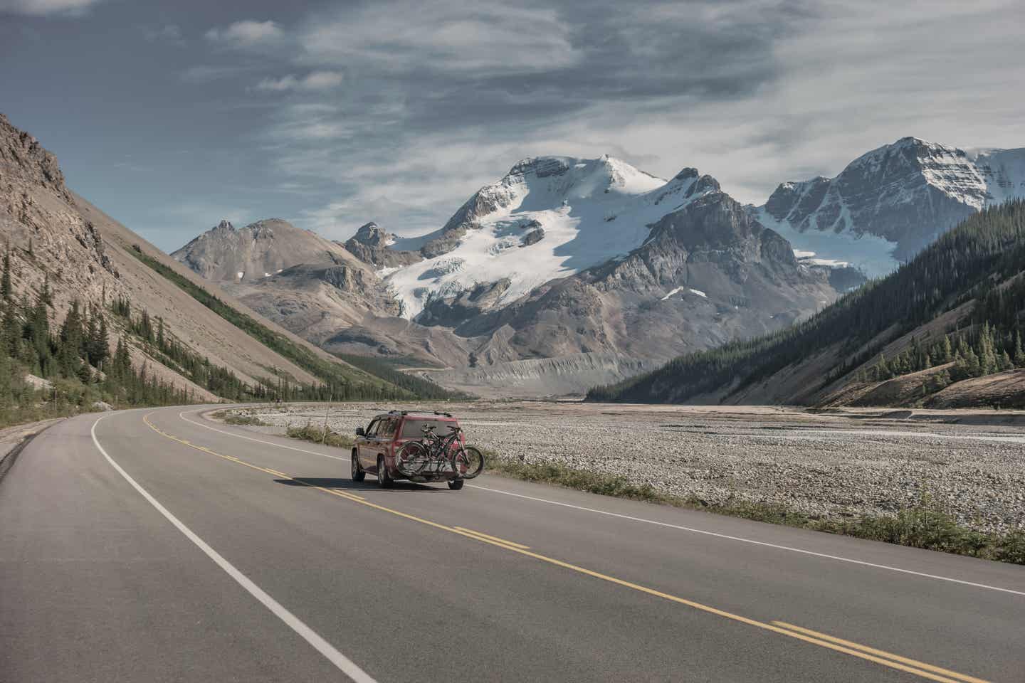 Alberta Urlaub mit DERTOUR. Auto mit Fahrrädern auf Gepäckträger fährt den Icefield Parkway entlang. Im Hintergrund der Mount Athabasca