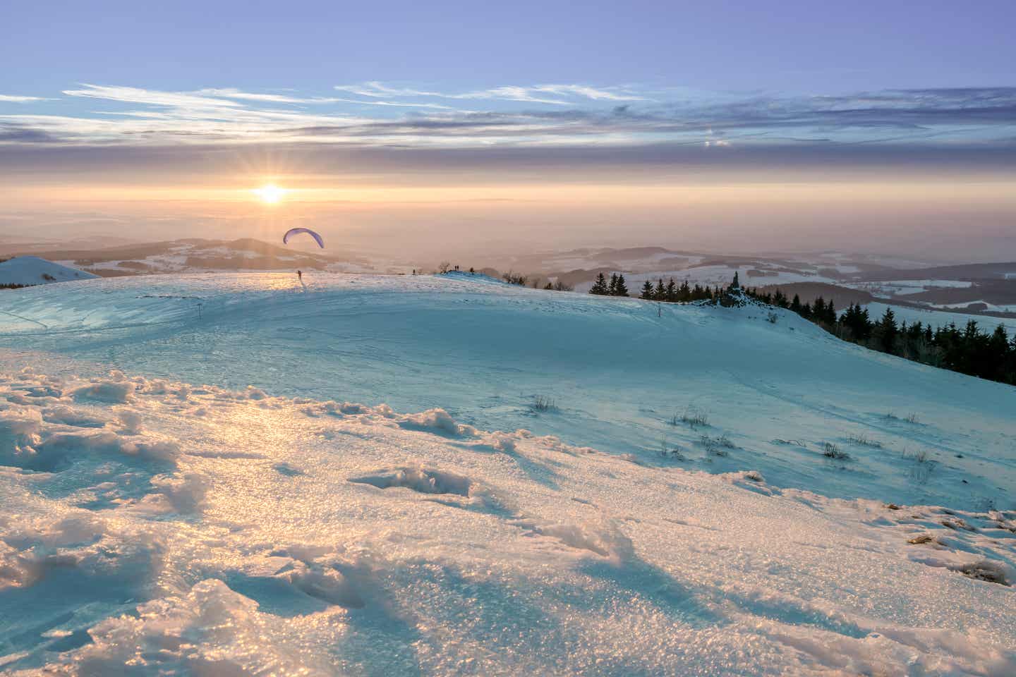 Rhön Urlaub mit DERTOUR. Gleitschirmflieger auf der verschneiten Wasserkuppe bei Sonnenaufgang