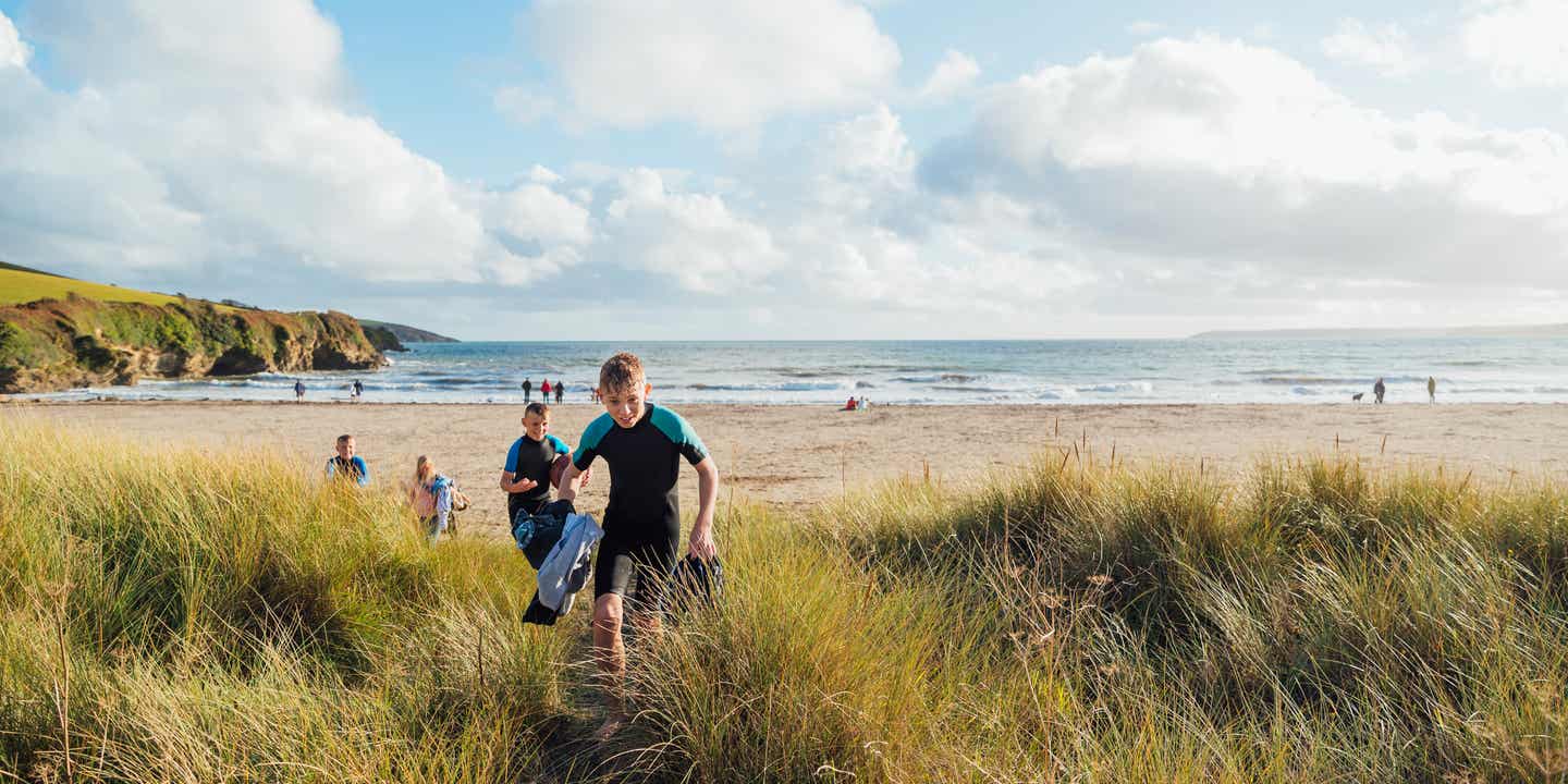 Jungen im Neoprenanzug rennen über die Dünen am Strand