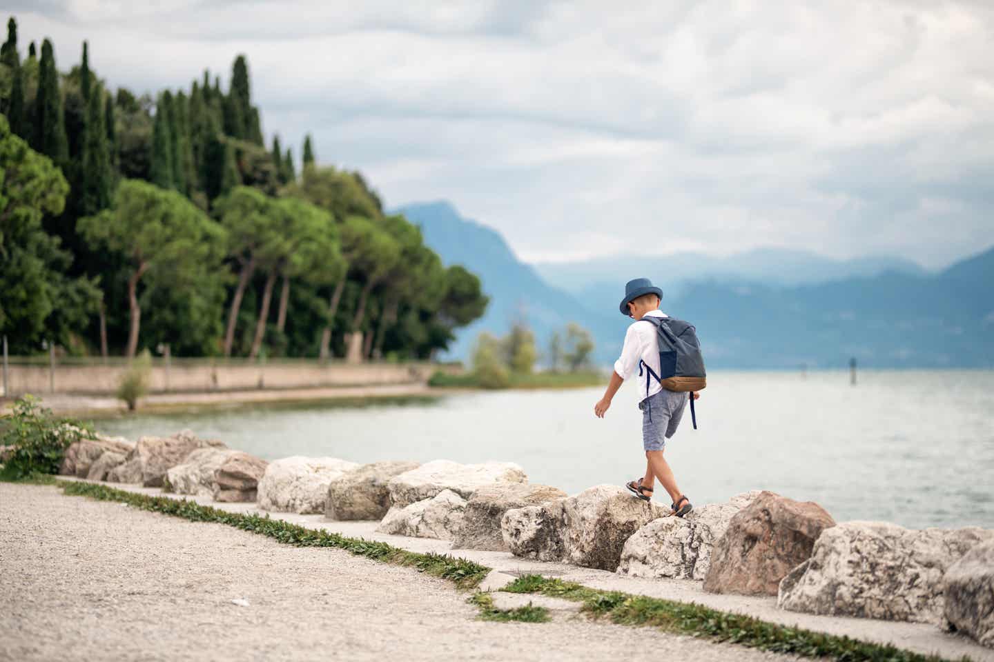 Kleiner Junge läuft auf Steinen am Ufer des Gardasees in Sirmione während eines Familienurlaubs am Gardasee