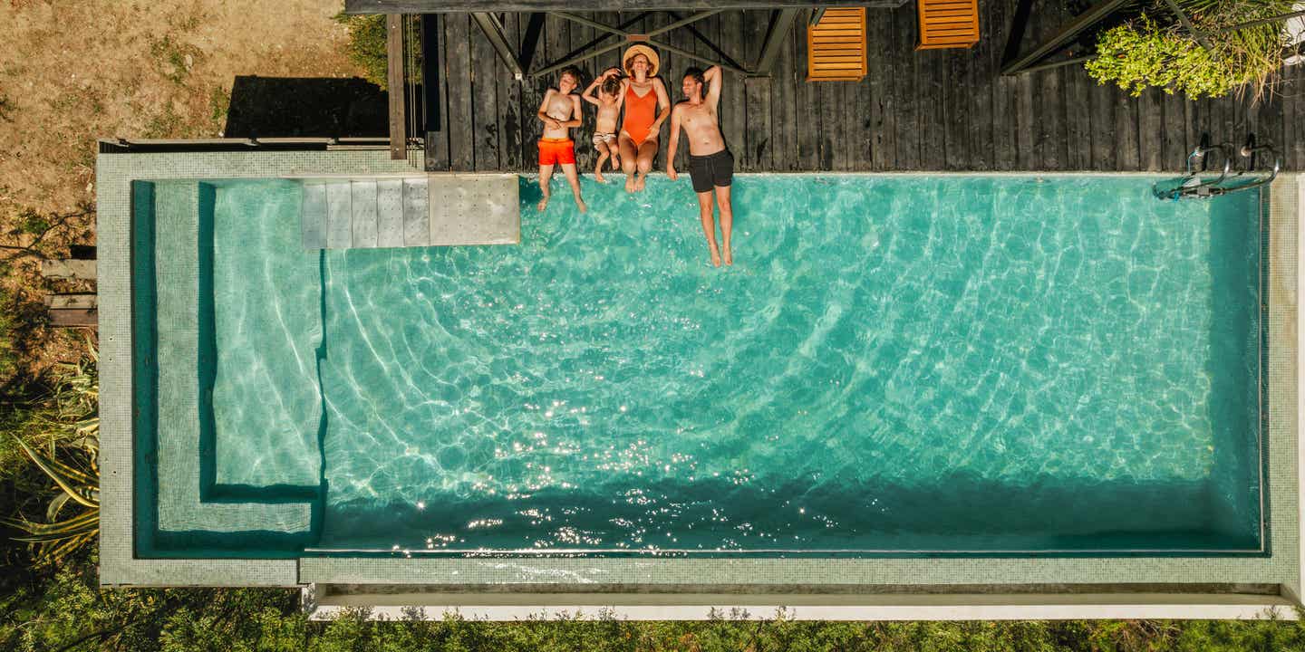 Luftaufnahme einer Familie, die entspannt am Poolrand liegt und die Sonne genießt