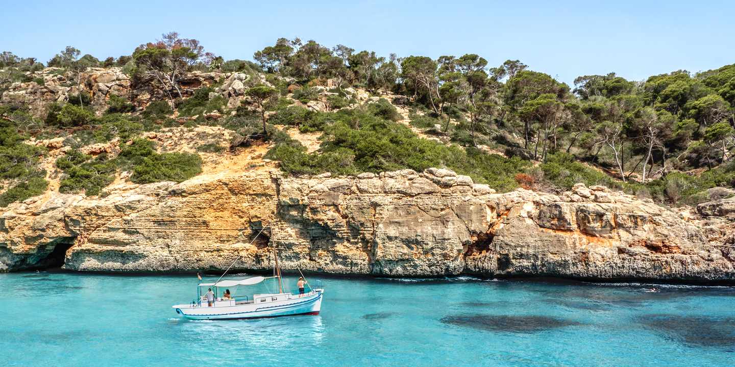 Segelboot vor Felsküste nahe Can Pastilla auf Mallorca in klarem Wasser, Badebucht mit Blick auf bewachsene Klippen