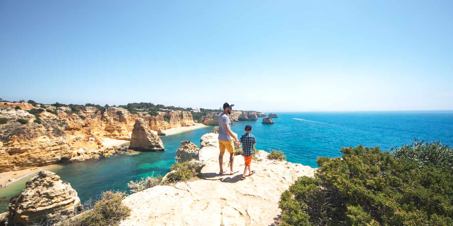 Vater und Sohn spazieren an Klippenküste der Algarve in Portugal mit Blick auf Meer und Felsen