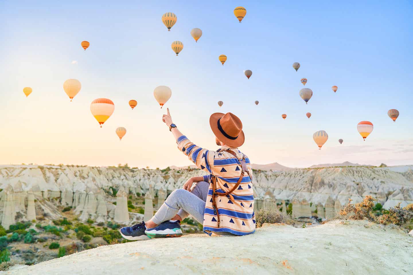 Mann zeigt auf Heißluftballons bei Sonnenaufgang in Kappadokien – Symbol für Main Character Energy beim Reisen