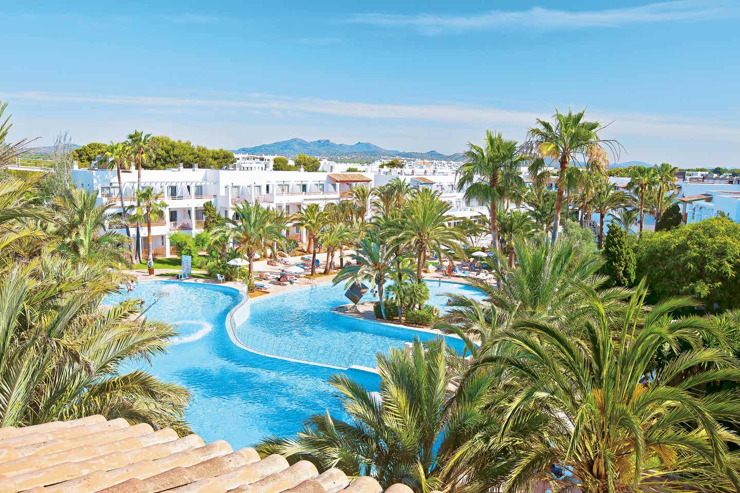 Poollandschaft des Calimera Fido Gardens auf Mallorca, umgeben von Palmen und weißen Gebäuden mit Blick auf die Hügel in der Ferne