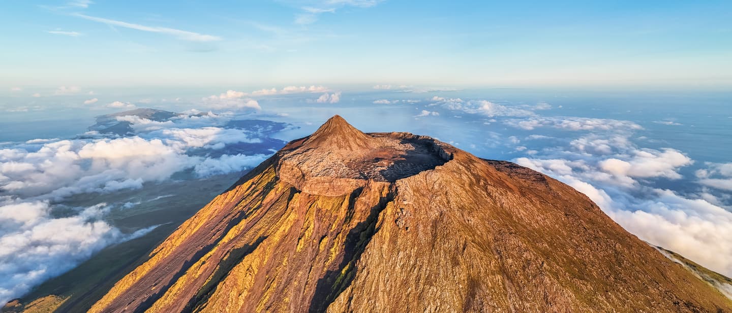 Eines der 7 Naturwunder Portugals: der Vulkan Pico auf den Azoren mit Krater und Wolkenmeer im warmen Licht der Abendsonne