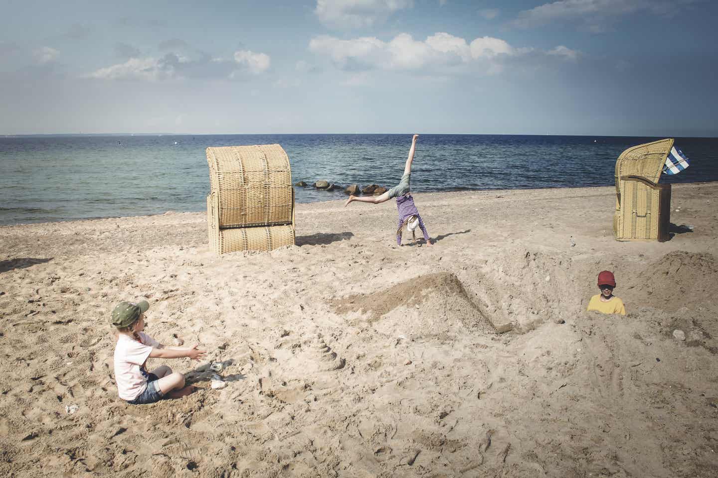 Travemünde Urlaub mit DERTOUR. Drei Kinder spielen am Strand zwischen zwei Strandkörben