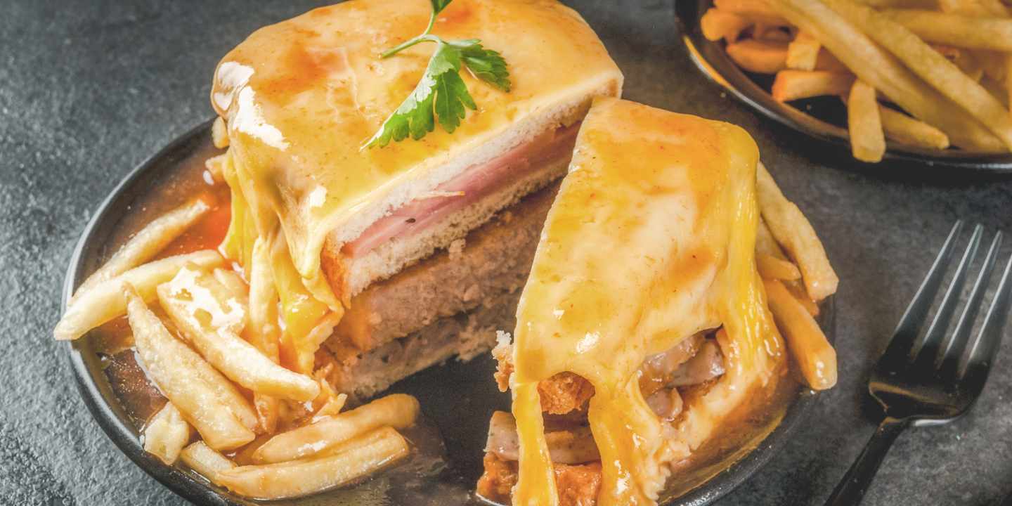 Porto Tipps – das Francesinha-Sandwich aus Porto mit geschmolzenem Käse, Fleischschichten, Sauce und Pommes auf Teller 