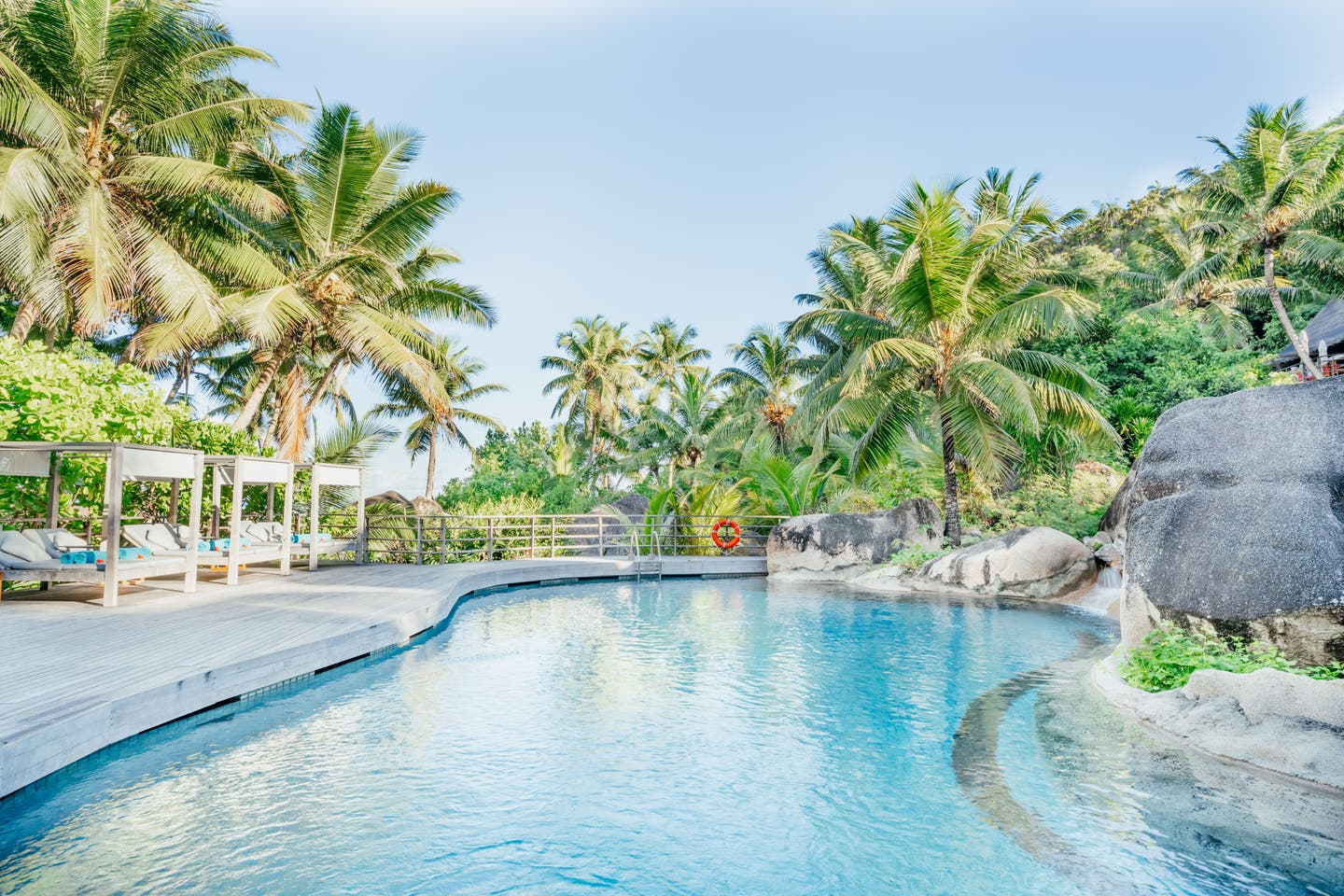 Pool mit Felsen und einer Sonnenterrasse vor Palmen