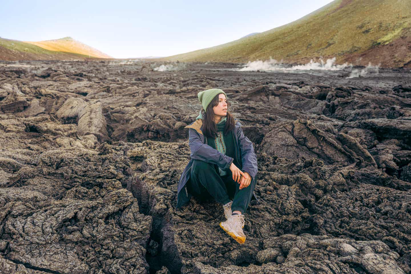 Frau mit Mütze sitzt auf erkalteter Lava am Vulkan Fagradalsfjall – Island als Kulisse für Main Character Energy Reisen