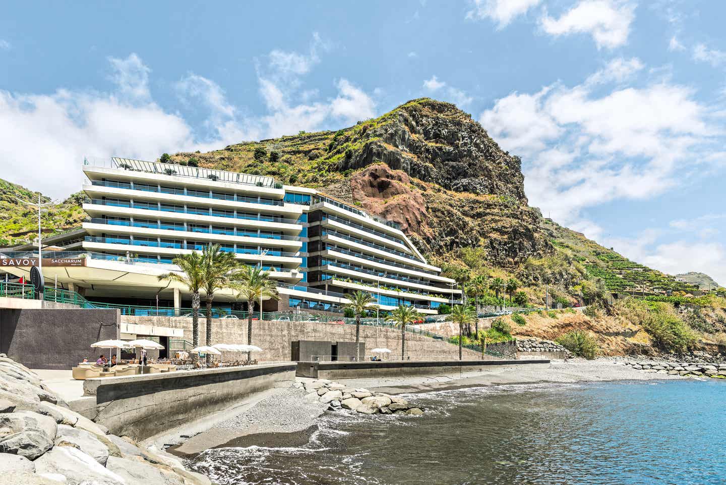 Blick auf den Hotelkomplex und Strand des Saccharum Resort auf Madeira, bewachsene Hügel im Hintergrund