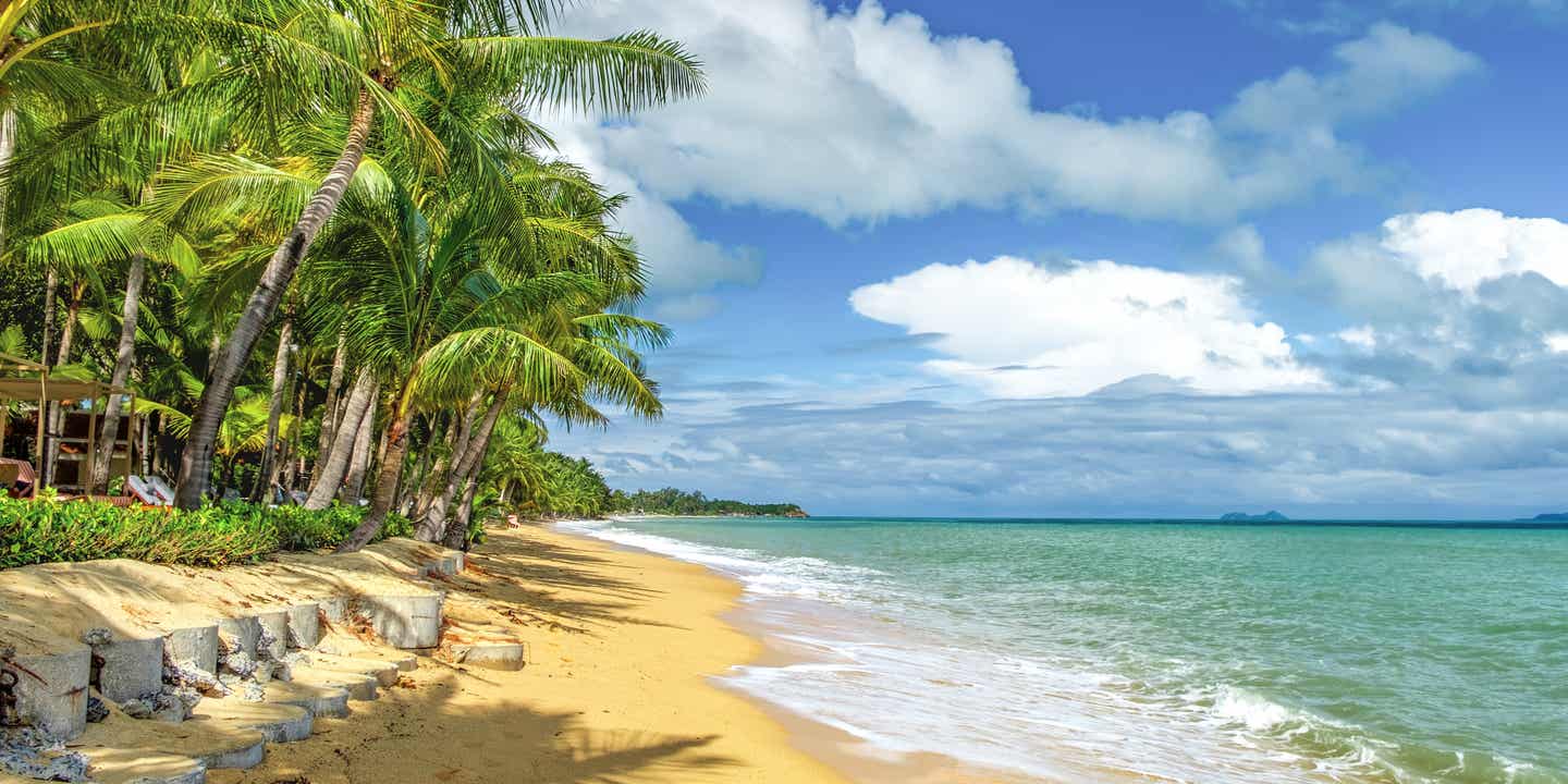 Maenam Beach, einer der Koh Samui Strände mit schmalem Sandstreifen, Palmen und Blick auf das ruhige Meer unter bewölktem Himmel