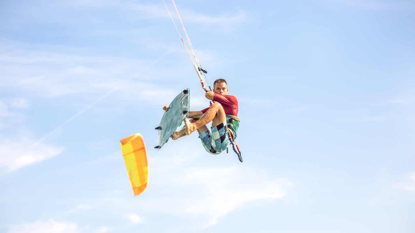 Kitesurfer springt mit Board in die Luft bei Tarifa – Trick unter blauem Himmel mit kräftigem Wind 