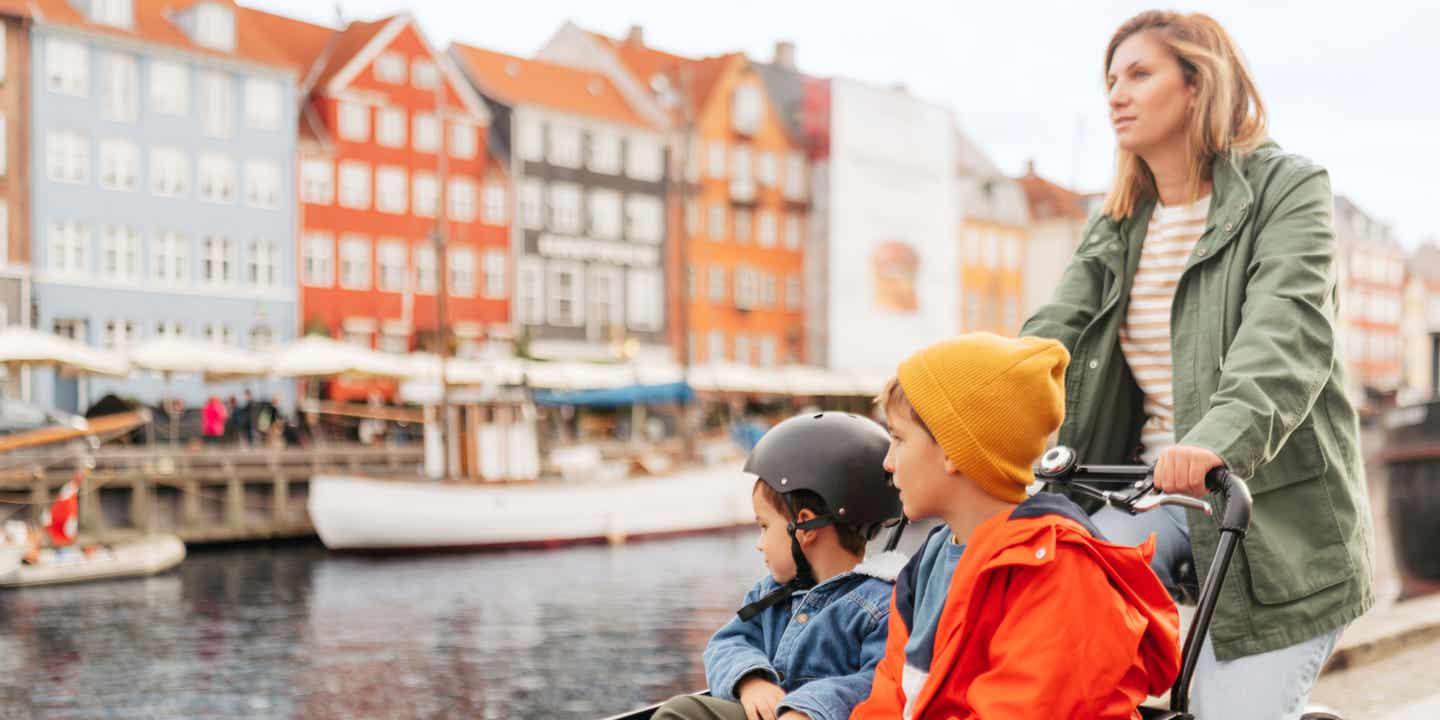 Eine Frau fährt mit zwei Kindern im lastenfahrrad am Nyhavn in Kopenhagen vorbei