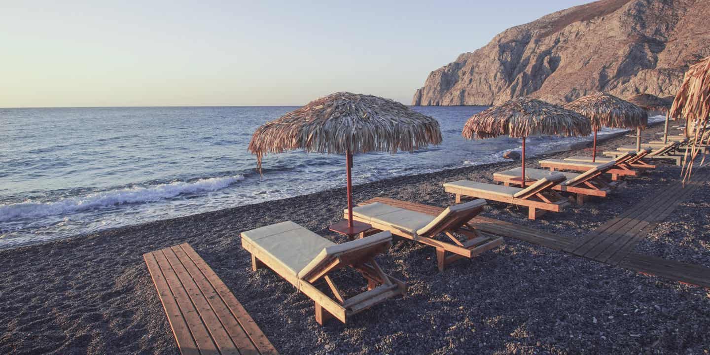 Santorinis Strände: Kamari Beach mit schwarzem Sand und Sonnenschirmen und Liegen