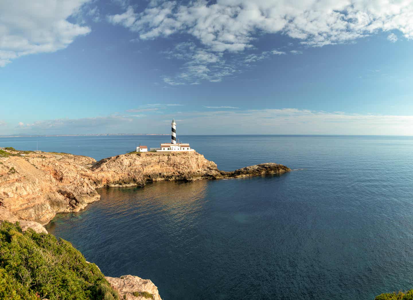 Weiß-blauer Leuchtturm auf einer felsigen Landzunge vom Meer umgeben