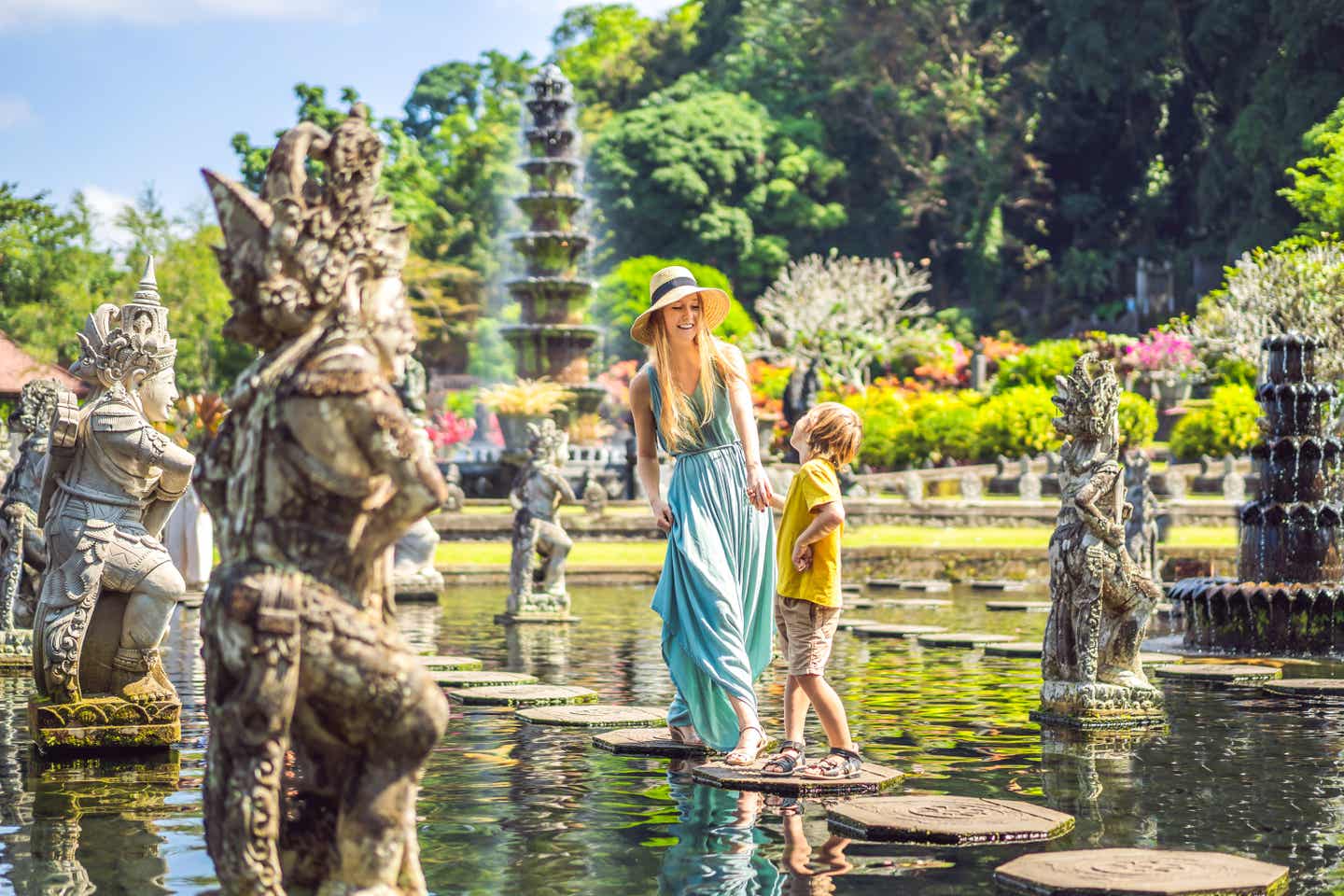 Touristische Mutter und Sohn im Wasserpalast Taman Tirtagangga, balancieren auf Trittsteinen auf einem Wasserbecken