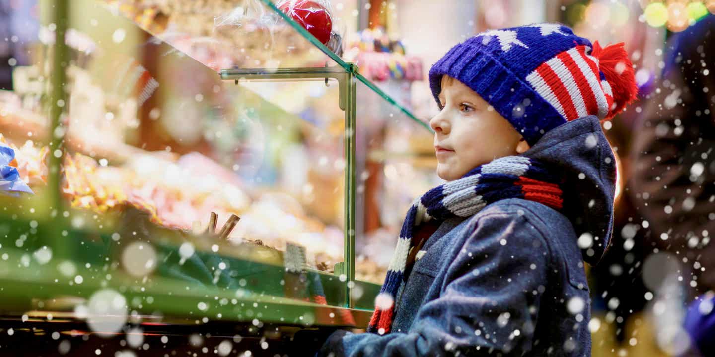 Ein kleiner Junge schaut auf die Auslage in einem Süßigkeitenstand auf dem Weihnachtsmarkt