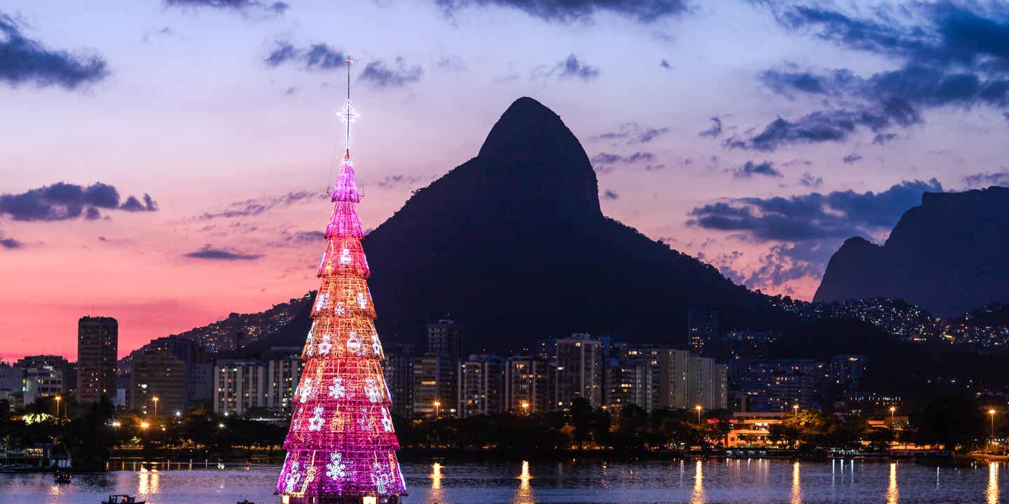 Blick auf einen erleuchteten Weihnachtsbaum auf dem Wasser am Strand mit dem Zuckerhut im Hintergrund
