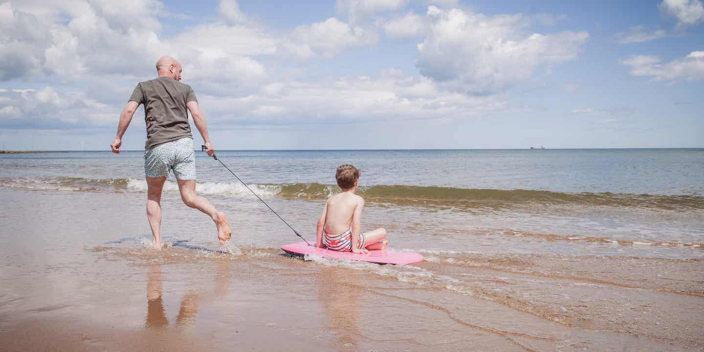 Familienurlaub Deutschland:Vater und Sohn spielen am Strand mit einem Surfbrett