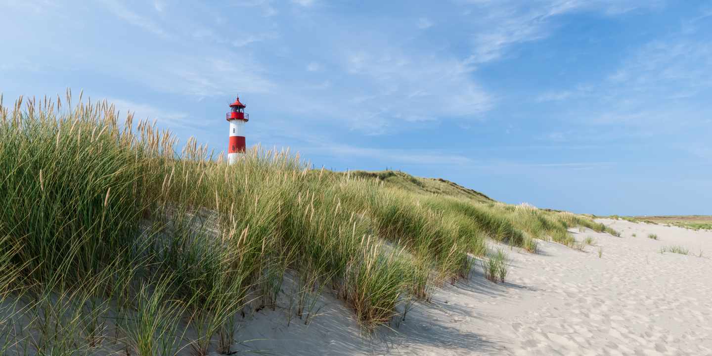 Ein rot-weiß-gestreifter Leuchtturm in den Dünen eines Strandes auf Sylt bei blauem Himmel