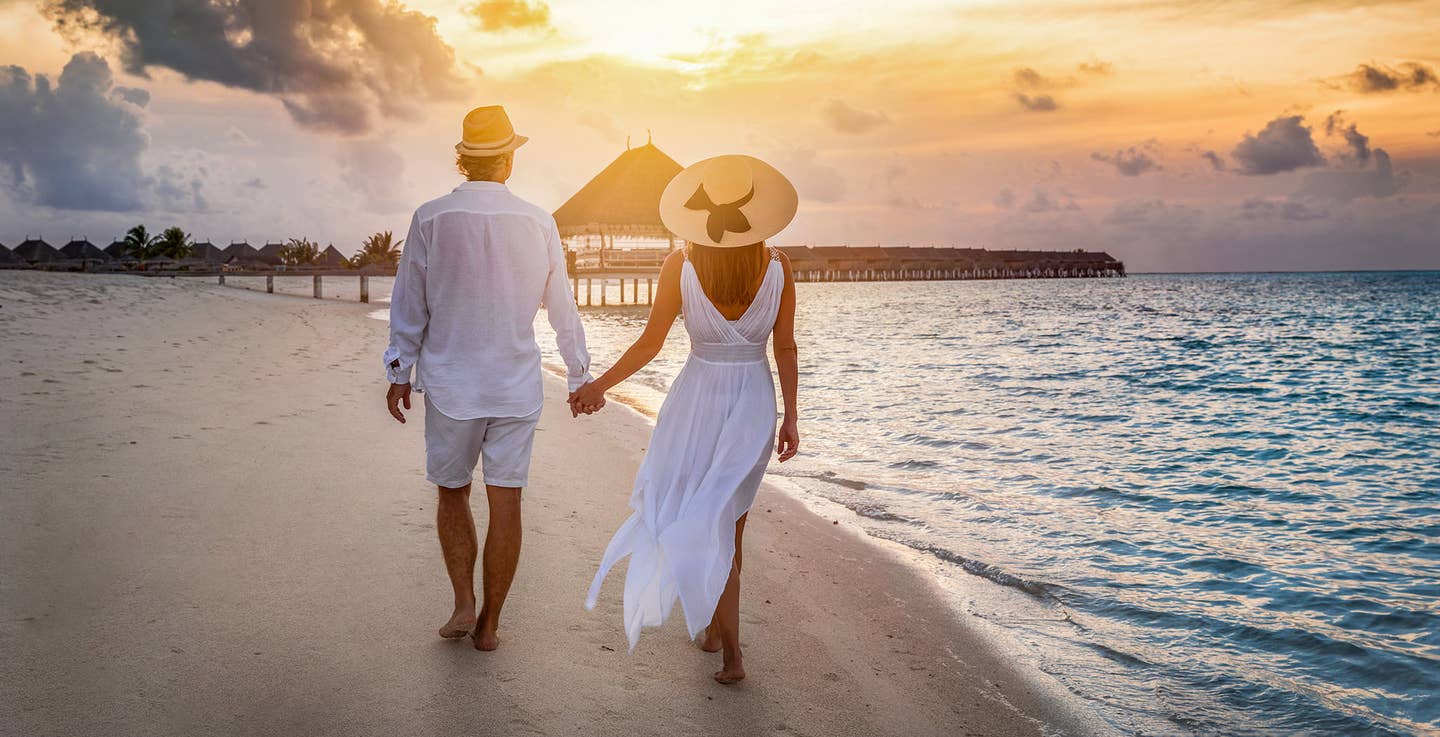 Paar spaziert bei Sonnenuntergang Hand in Hand am Strand auf den Malediven