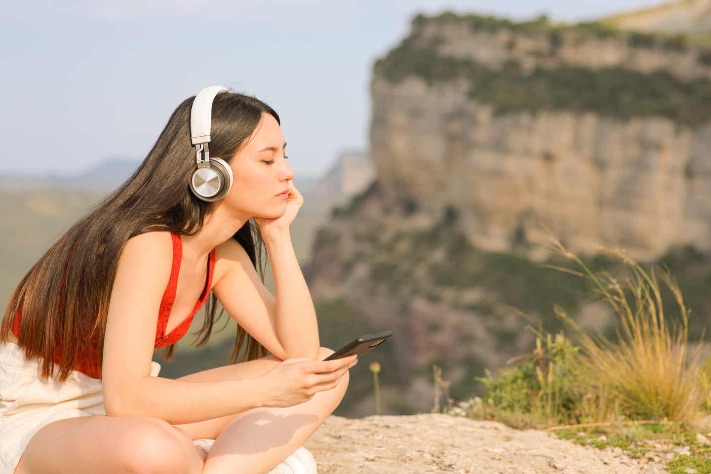 Frau mit Kopfhörern entspannt beim Musikhören in der Natur – Main Character Energy beim Reisen