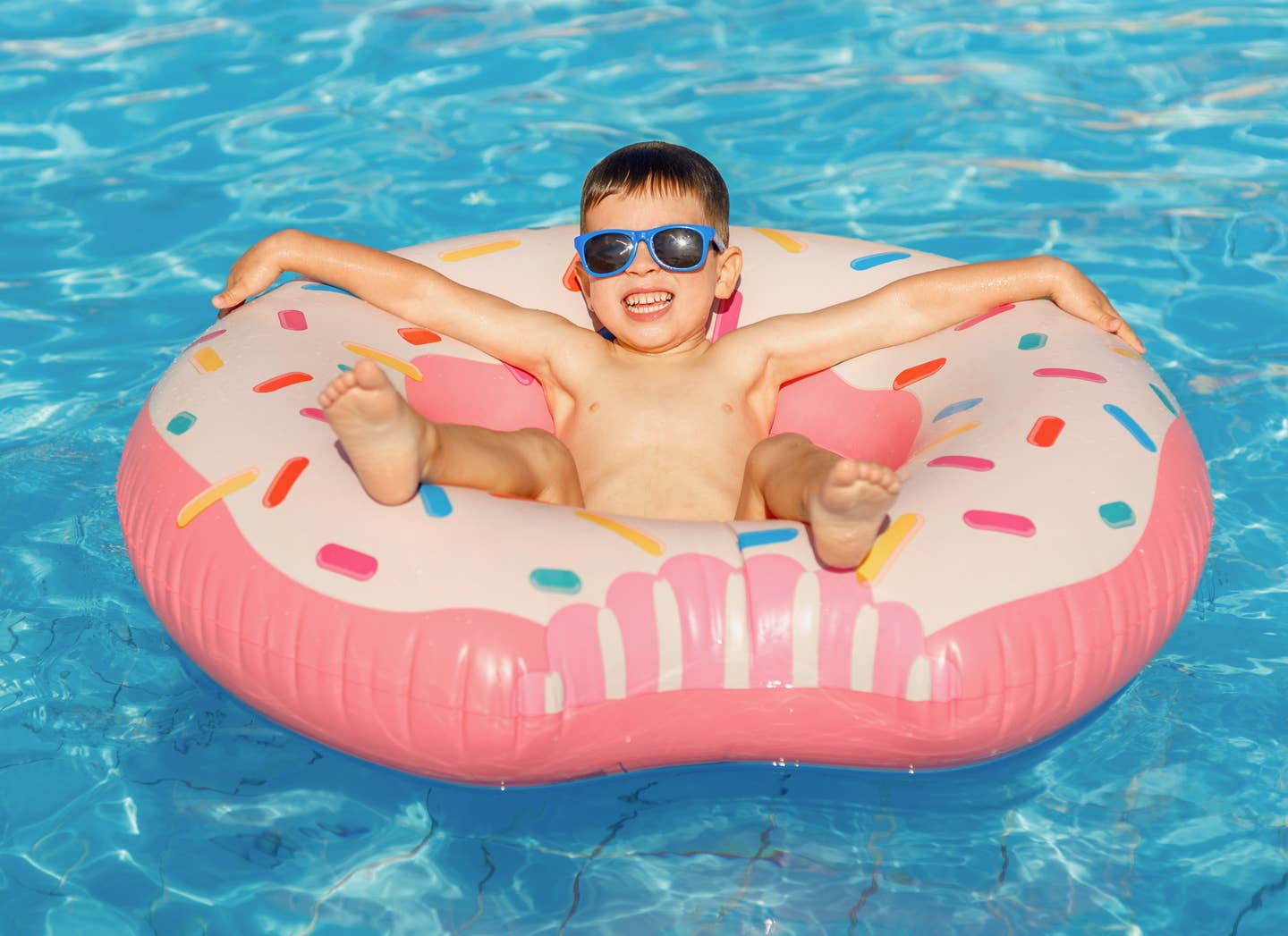 Ein Junge mit Sonnenbrille treibt in einem Donutring in einem Hotelpool