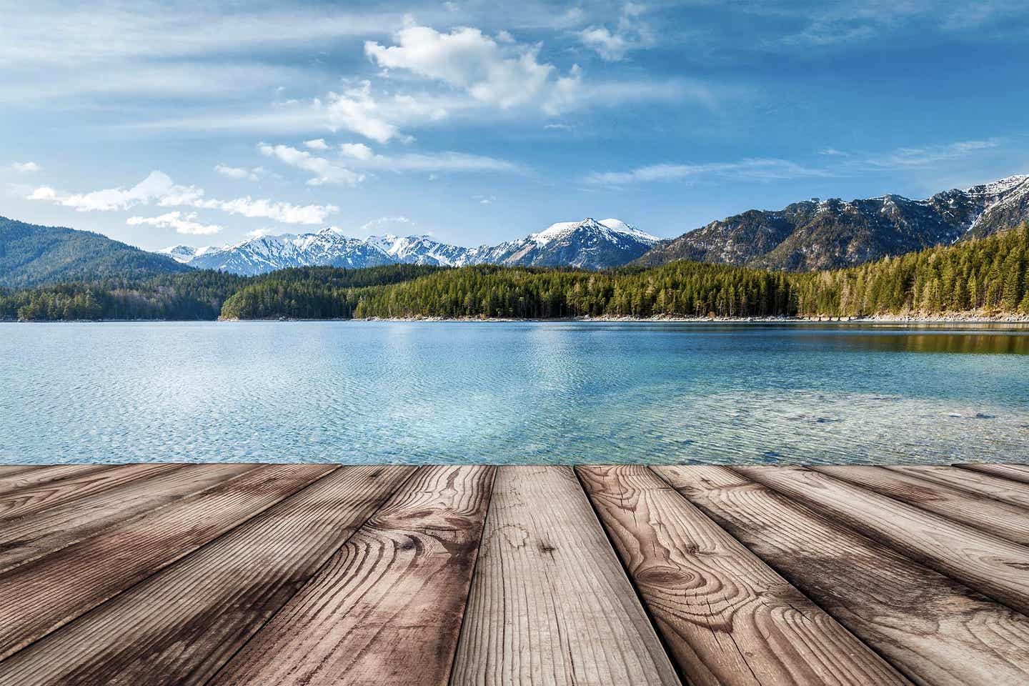 Ein glasklarer Badesee mit Steg und Alpenpanorama im Hintergrund