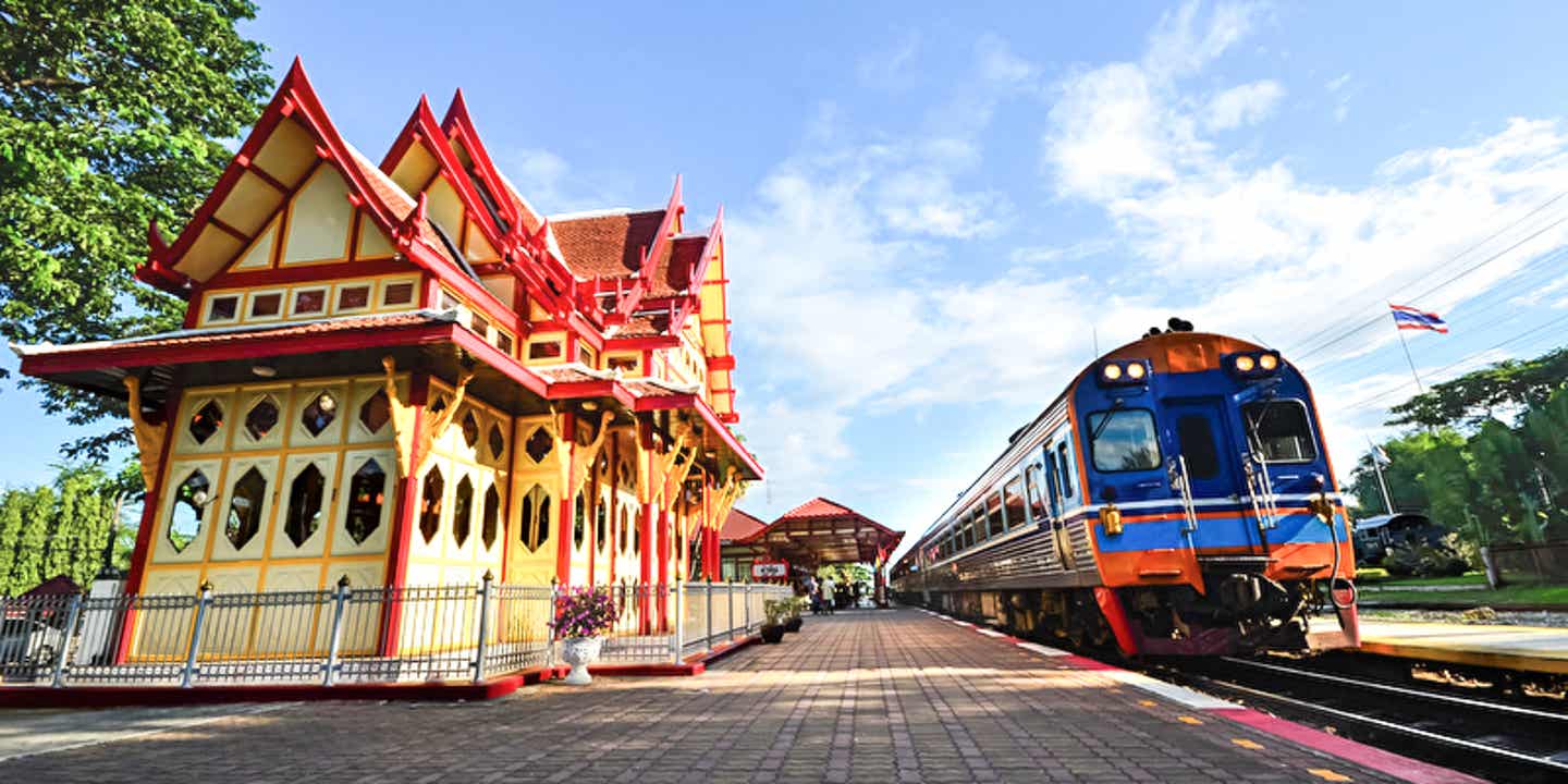 Blick auf einen Bahnhof in Thailand mit typischer Architektur und einem Zug auf dem Gleis wartend