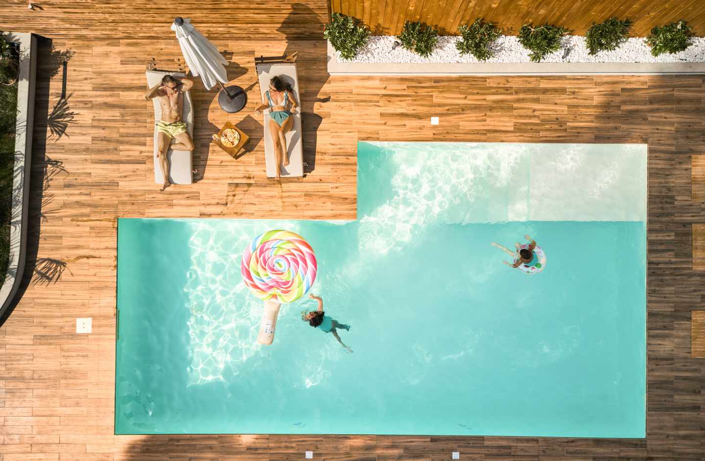 Junge Familie verbringt einen entspannten Sommertag in den Herbstferien am Pool mit Luftmatratzen 