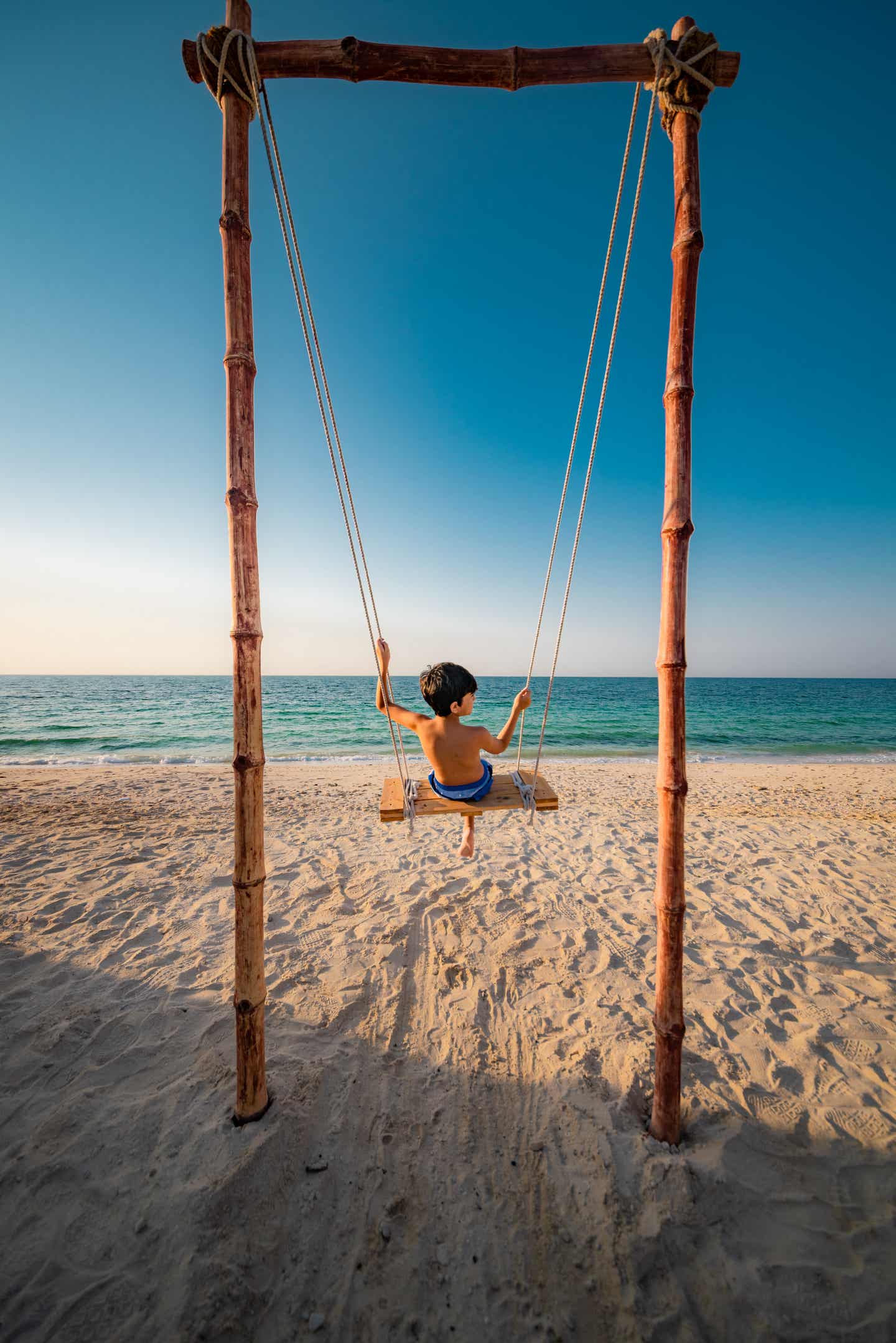 Kind sitzt auf Schaukel am Strand von Ajman