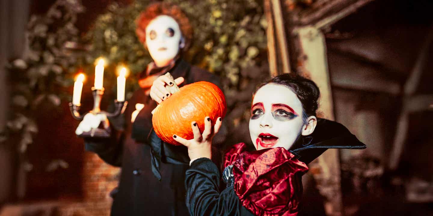 Verkleidete Kinder feiern Halloween mit großem Kürbis in den Händen