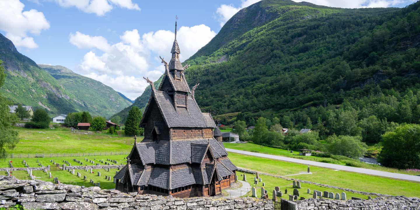 Die historische Borgund Stabkirche in Norwegen aus dem Jahr 1180, umgeben von grüner Sommerlandschaft und Bergen