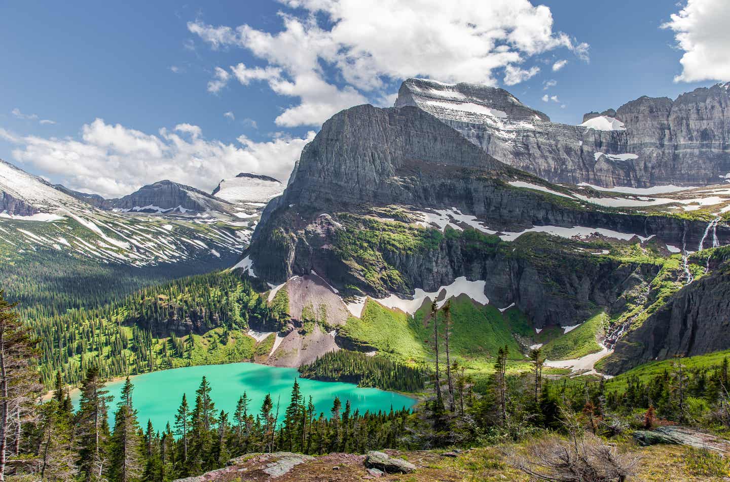 Blick auf das Tal des Glacier Nationalparks in den Rocky Mountains mit Gebirgsketten, dichten Bäumen und dem Grinnell See