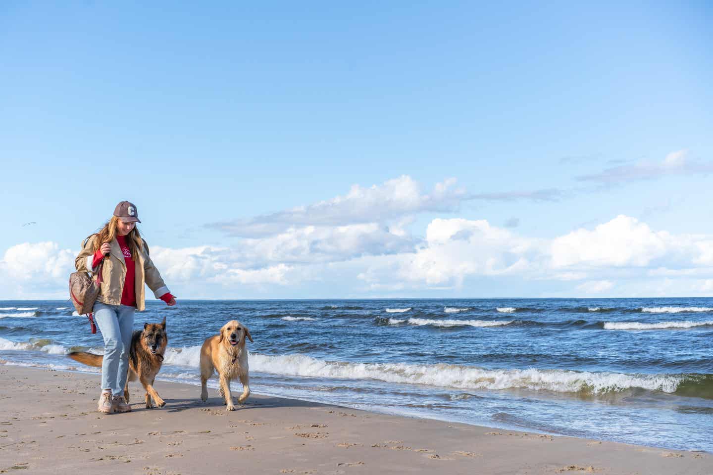 Frau spaziert mit zwei Hunden am Strand bei sonnigem Wetter – ein perfekter Moment im Urlaub mit Hund an der Ostsee