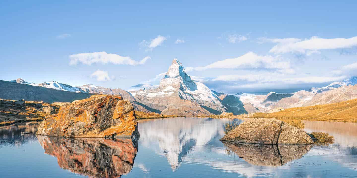 Berg mit Schnee vor Wasser, spiegelt sich im Wasser, blauer Himmel