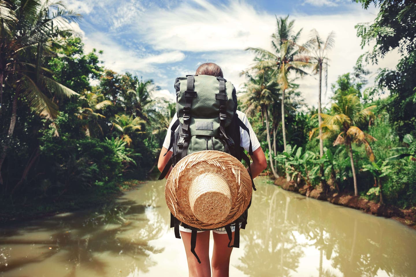 Reisemagazin Insider-Tipps: Frau mit Rucksack steht im Dschungel vor einem Fluss