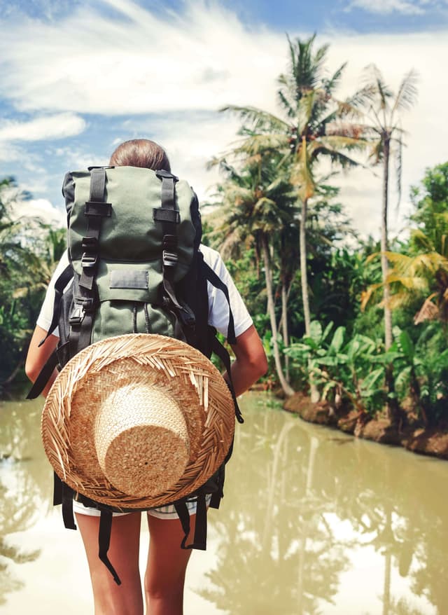 Insider-Tipps Reisemagazin Insider-Tipps: Frau mit Rucksack steht im Dschungel vor einem Fluss