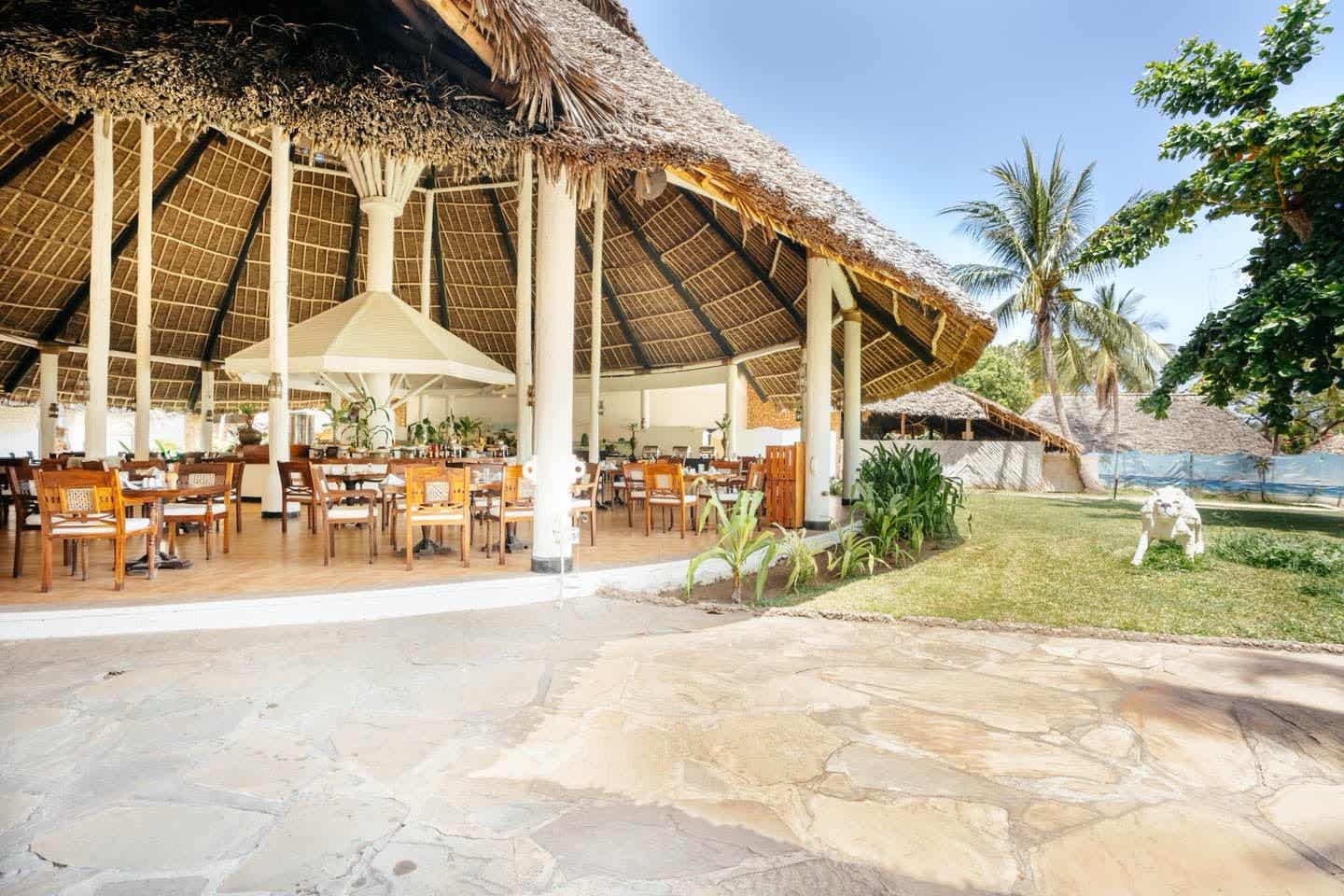 Genuss unter Palmdach – Restaurant im ananea Diamonds Malind in Kenia Offenes Restaurant im ananea Diamonds Malindi mit traditionellem Makuti-Dach, Holzmöbeln und tropischem Garten an Kenias Küste
