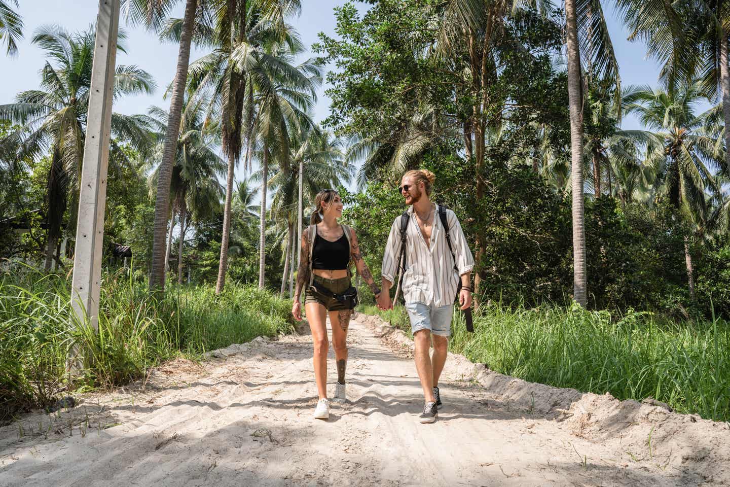 Ein Paar spaziert auf einem Sandweg vor Palmen