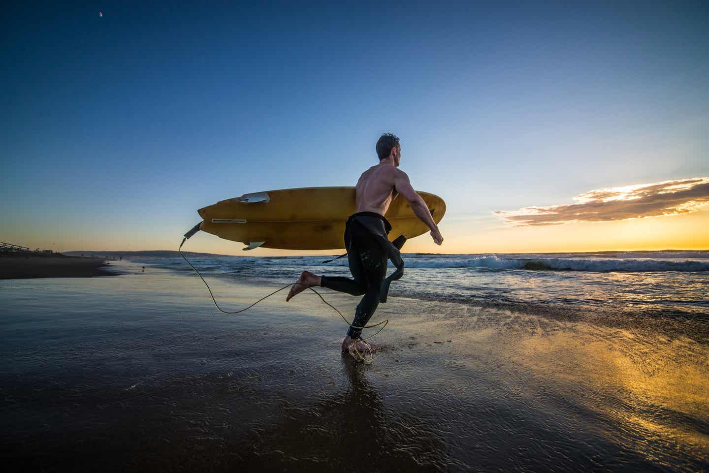 Ein begeisterter Surfer geht mit Surfbrett unter dem Arm ins Meer, um die Wellen während seines Los-Angeles-Urlaubs zu erobern.