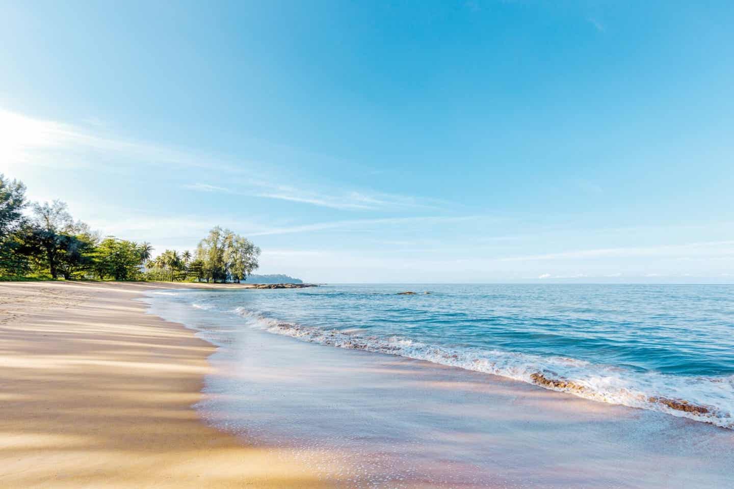 Blick auf den Khuk Khak Strand in Khao Lak mit Holzliegen und Palmen