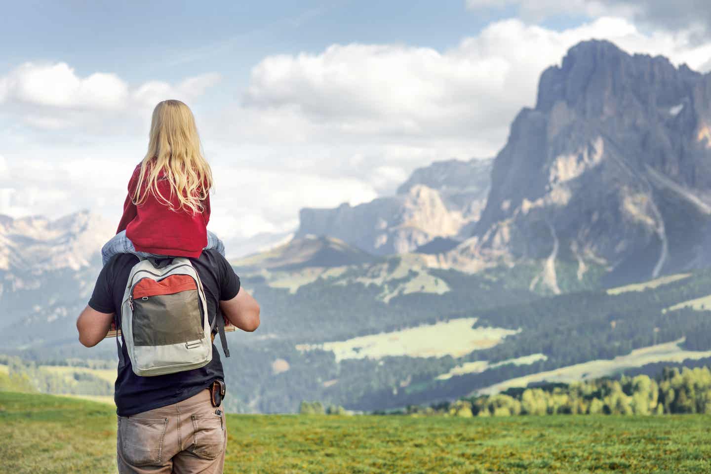 Südtirol Urlaub mit DERTOUR. Vater mit Tochter auf den Schultern. Beide betrachten das Bergpanorama der Dolomiten