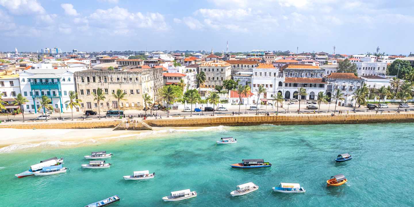Stone Towns Altstadt mit historischen Gebäuden, Palmen und vielen kleinen Booten im klaren Küstenwasser von Sansibar