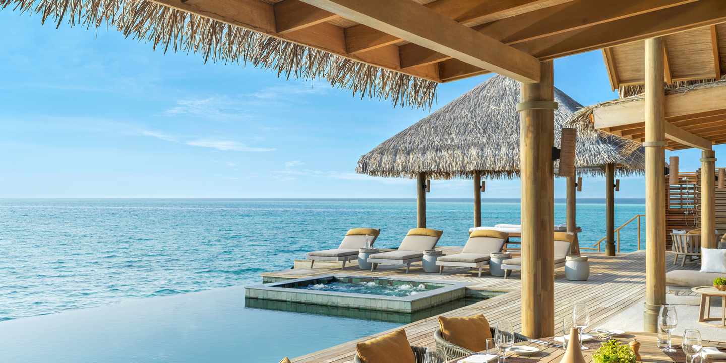 Liegestühle mit Kissen auf Holzsteg neben Pool und Meer unter Strohdach im Vakkaru Maldives