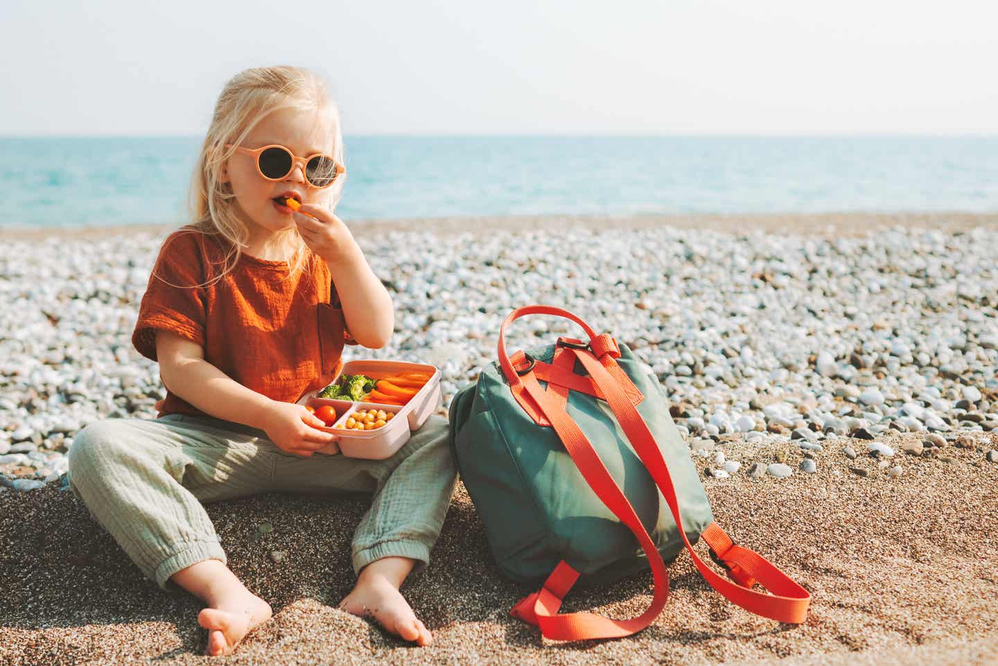 Packliste für den Urlaub mit Kindern: Ein Kind isst gesunde Gemüse-Snacks am Strand.